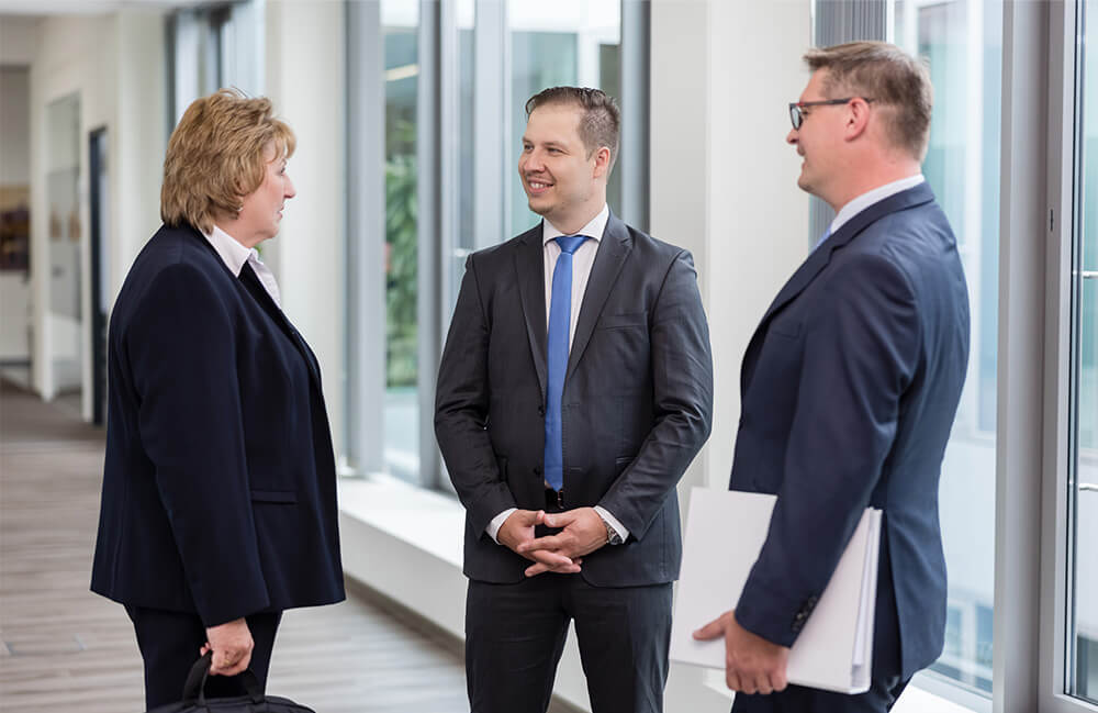 Drei Mitarbeitende stehen im Gang der Unigarant und unterhalten sich. 