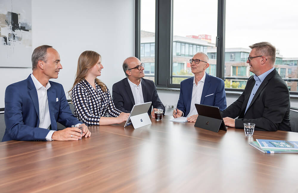 Die fünf Partner der Unigarant sitzen an einem Konferenztisch und unterhalten sich.